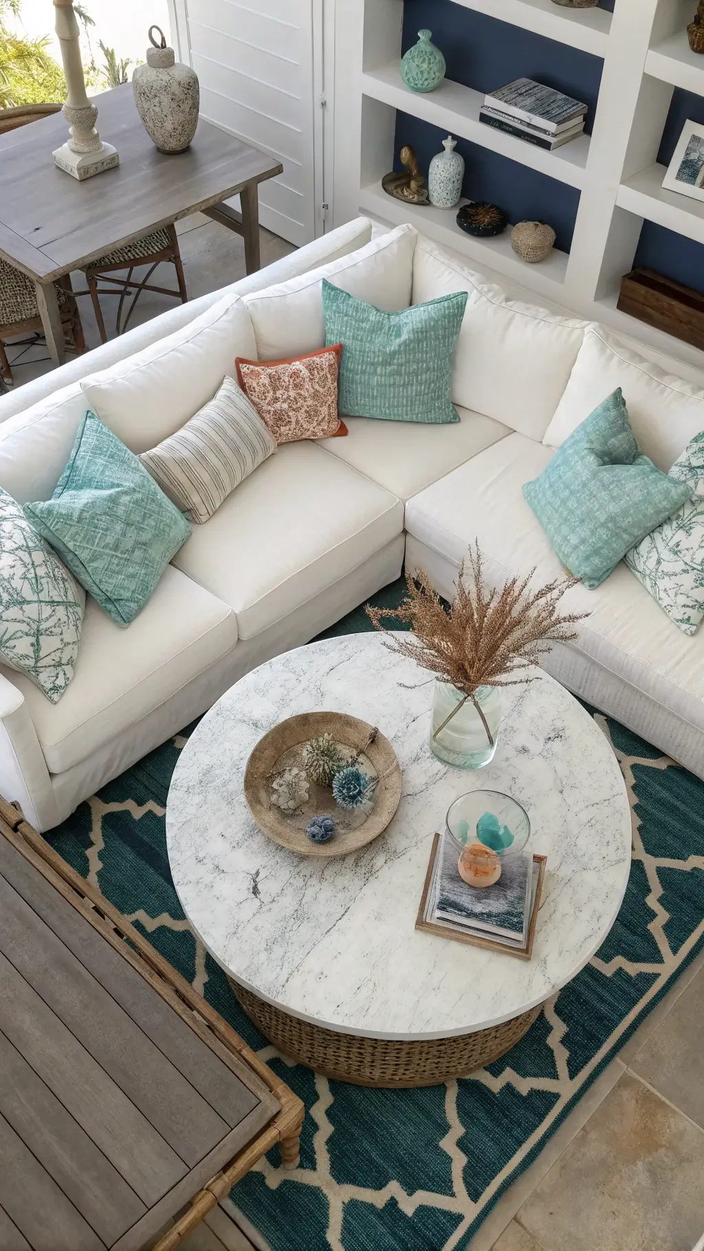 Aerial view of conversation area with white linen sectional, round marble coffee table with glass hurricane and coral, floating shelves with vintage textiles
